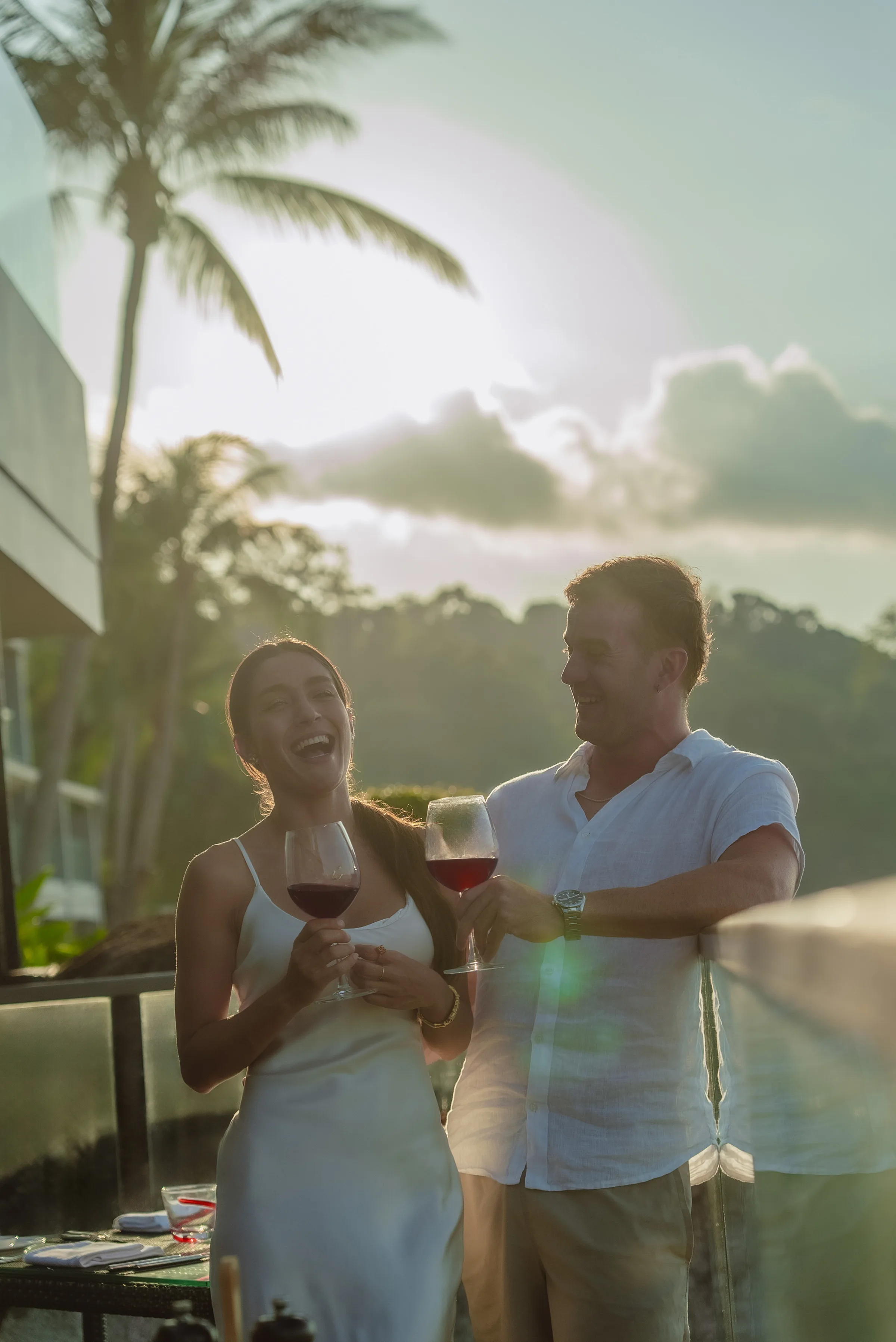 Joyful couple sharing laughter over wine with golden sunset lens flare