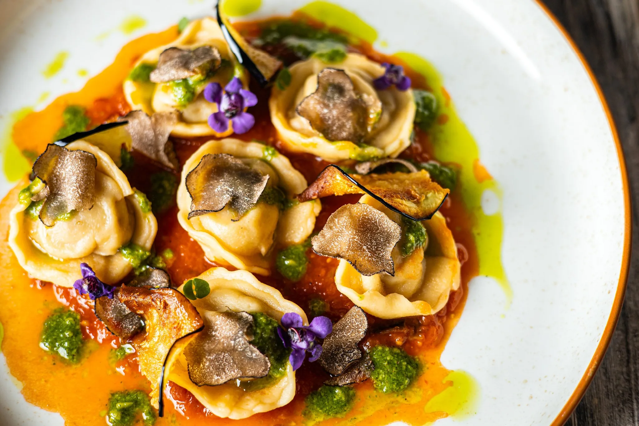 Handmade tortelli with truffle sauce and edible violet flowers